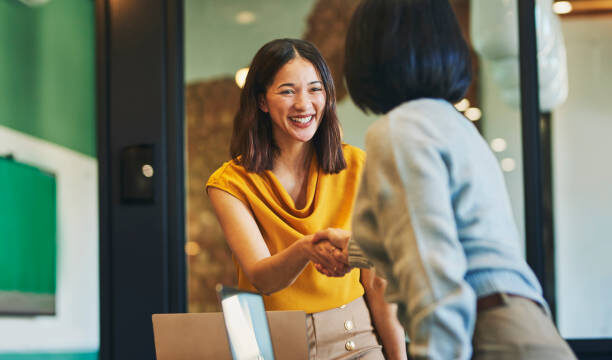 Businesswoman shaking hands with client and smiling cheerfully in meeting room